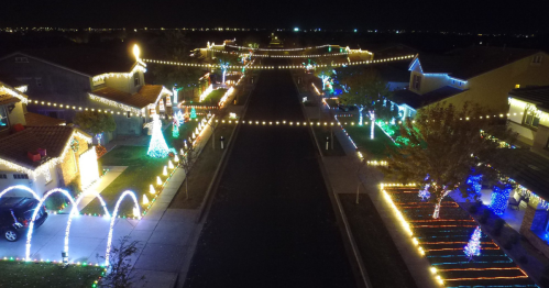 A festive neighborhood street illuminated with colorful holiday lights and decorations at night.