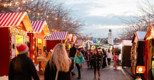 A festive market scene with colorful stalls, holiday lights, and people walking in winter attire.