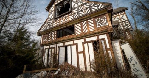 An abandoned house with a distinctive wooden frame and overgrown vegetation surrounding it.