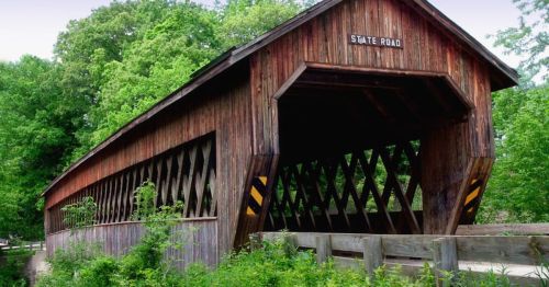 A wooden covered bridge with a sign reading "State Road," surrounded by lush green trees.