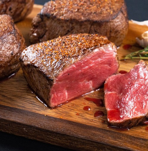 A close-up of a perfectly cooked steak, showcasing a juicy pink center and a seasoned crust, on a wooden platter.