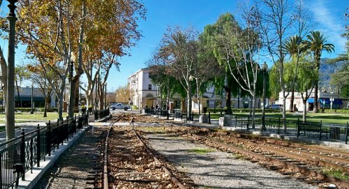 A view of a park with train tracks, trees, and buildings under a clear blue sky.