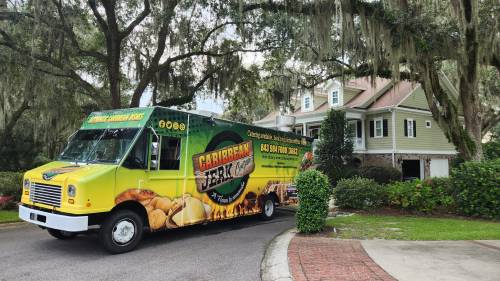 A colorful food truck parked near a house, promoting Caribbean jerk cuisine with vibrant graphics.