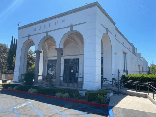 Exterior of a white museum building with arched entrances and a clear blue sky.