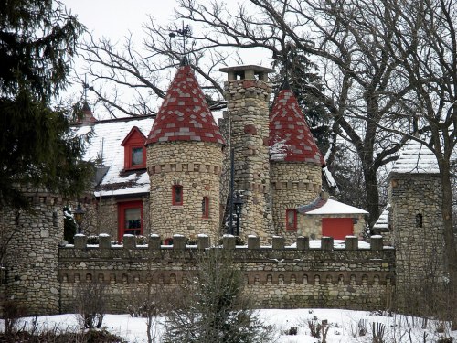 A stone castle with red roofs and turrets, surrounded by snow-covered trees and a winter landscape.
