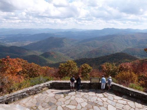 A scenic view of colorful autumn mountains with visitors at a lookout point.