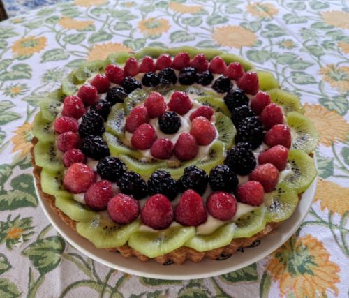 A colorful fruit tart topped with kiwi, raspberries, blackberries, and strawberries, arranged in a spiral pattern.