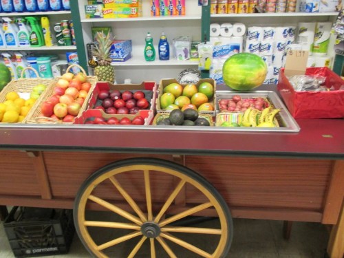 A wooden cart displaying a variety of fresh fruits, including apples, bananas, avocados, and a watermelon.