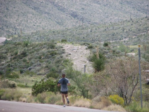 A person jogging on a road with a hilly, green landscape in the background.