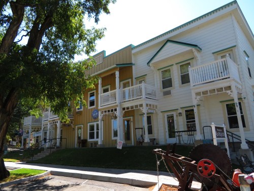 A row of charming, two-story buildings with balconies, set against a clear blue sky and green trees.