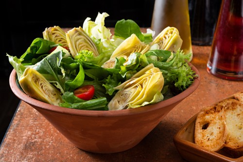 A bowl of fresh salad with artichoke hearts, mixed greens, and cherry tomatoes on a rustic table.