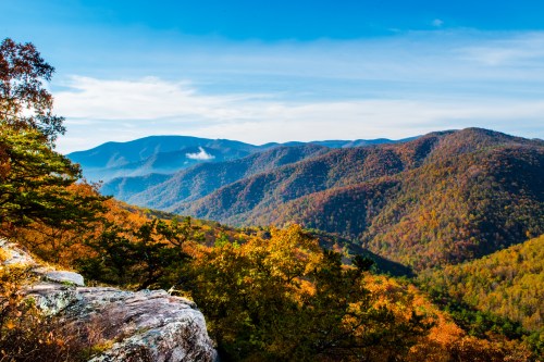 A scenic view of rolling mountains covered in autumn foliage under a clear blue sky.