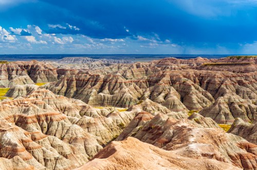 Vast, colorful badlands landscape with layered rock formations under a dramatic sky.