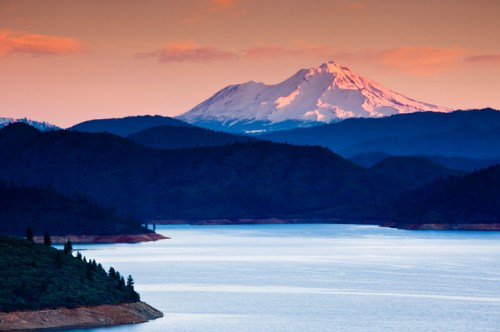 A serene lake surrounded by mountains at sunset, with a snow-capped peak in the background.