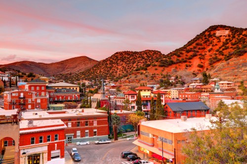 A scenic view of a colorful town nestled among mountains at sunset, with historic buildings and vibrant skies.