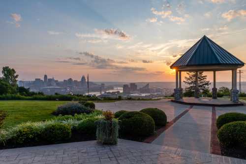 A scenic view of a city skyline at sunset, with a gazebo in the foreground and lush greenery surrounding the area.