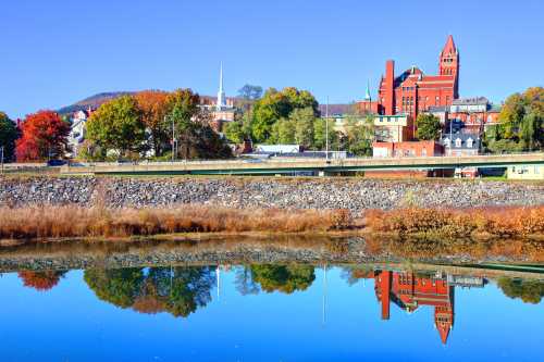 A scenic view of a town with colorful autumn trees, a river reflecting buildings, and a clear blue sky.