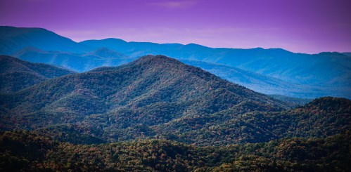 A panoramic view of rolling mountains under a purple sky, showcasing lush greenery and distant peaks.