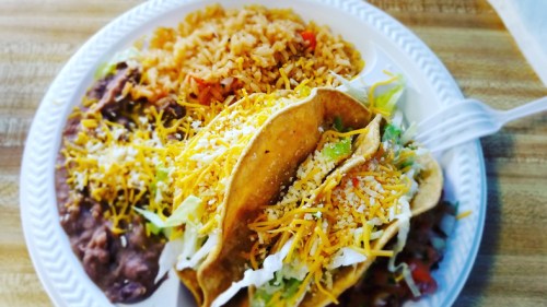 A plate of tacos filled with lettuce, cheese, and salsa, served with rice and refried beans.