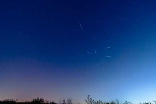 A clear night sky filled with stars, featuring several bright streaks, likely meteor trails, against a deep blue backdrop.