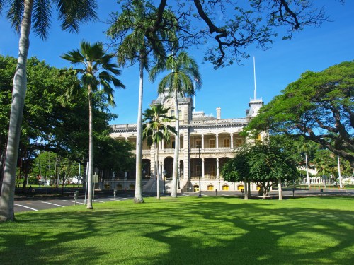 Historic building surrounded by lush greenery and palm trees under a clear blue sky.
