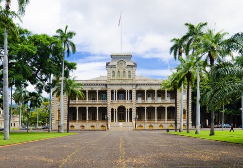 Historic building with a grand facade, surrounded by palm trees and a clear blue sky.