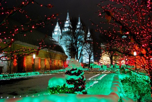 A snowy landscape illuminated by colorful lights, featuring a tall, ornate building in the background.