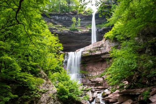 A serene waterfall cascades down rocky cliffs, surrounded by lush green trees and vibrant foliage.