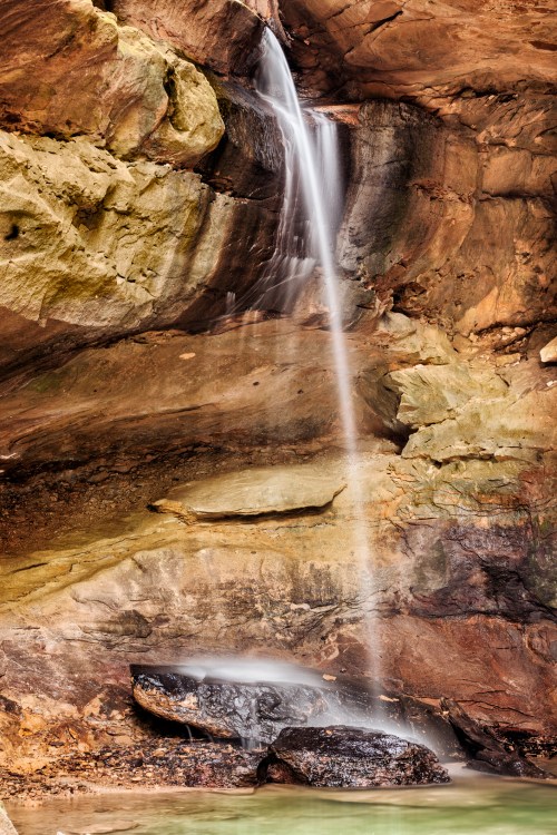 A serene waterfall cascading down a rocky cliff into a calm pool below, surrounded by textured stone walls.