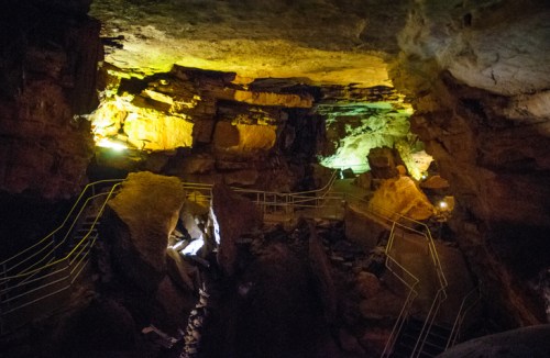 A dimly lit cave interior with colorful lights illuminating rock formations and a winding pathway.
