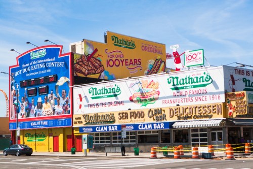 Colorful Nathan's Famous restaurant and contest venue, featuring signs for hot dogs and seafood, in a lively urban setting.