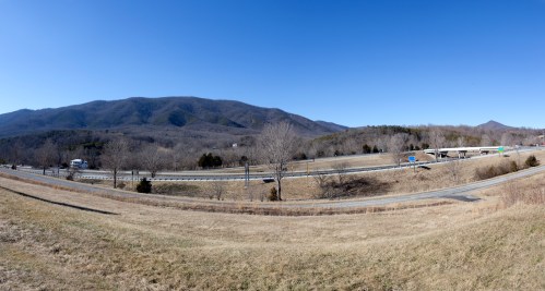 A panoramic view of a highway winding through a mountainous landscape under a clear blue sky.