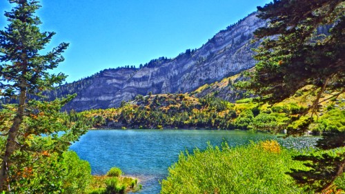 A serene lake surrounded by lush greenery and towering mountains under a clear blue sky.