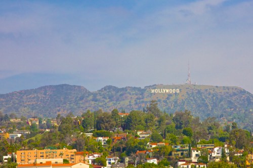 View of the Hollywood sign on a hillside, surrounded by greenery and residential buildings under a clear blue sky.