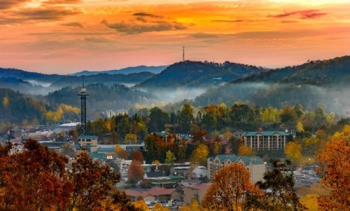 A scenic view of a mountain town at sunset, with colorful autumn foliage and misty hills in the background.