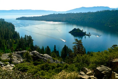 A serene lake surrounded by lush forests and mountains, with boats gliding across the water under a clear sky.