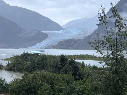 A serene landscape featuring a glacier, mountains, and a calm lake surrounded by lush greenery.