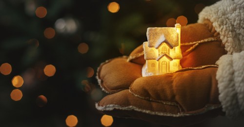 Hands holding a tiny lit house.