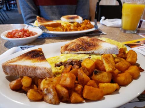A plate of breakfast featuring an omelette with toast and golden-brown home fries, with a side of salsa and orange juice.