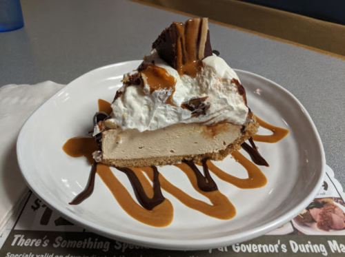 A slice of dessert pie topped with whipped cream, chocolate drizzle, and caramel on a white plate.