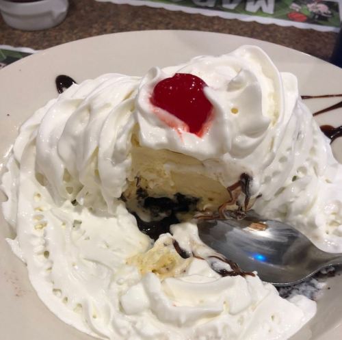 A dessert with whipped cream, a cherry on top, and a spoon, revealing layers of ice cream and chocolate sauce.