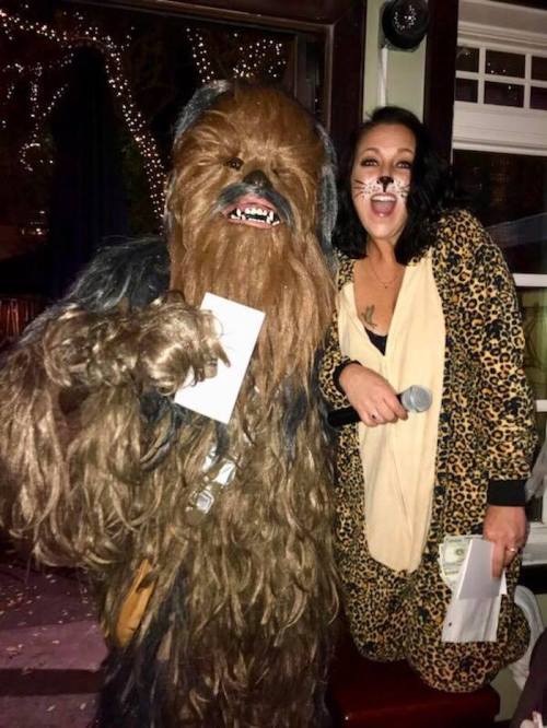A person in a Chewbacca costume poses with a woman in a leopard print outfit, both smiling at a festive event.