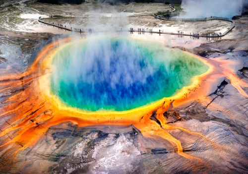 Aerial view of Yellowstone's Grand Prismatic Spring, showcasing vibrant blue, green, and orange colors with steam rising.