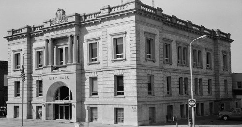 Historic city hall building with a grand facade, featuring large windows and an arched entrance, in black and white.