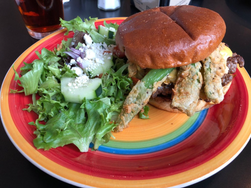 A colorful plate featuring a burger with toppings and a side salad of greens, cucumber, and feta cheese.