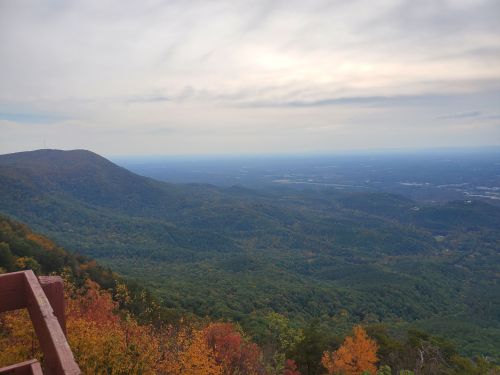 A panoramic view of rolling mountains and valleys, showcasing autumn foliage under a cloudy sky.