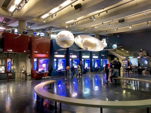 A science museum exhibit featuring planets, interactive displays, and visitors exploring the space-themed installations.