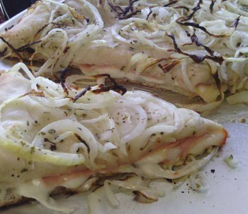 Slices of pizza topped with melted cheese, ham, and caramelized onions, garnished with herbs.
