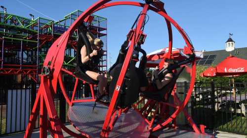 Two people are seated in a red amusement ride, preparing for a thrilling experience at an outdoor amusement park.