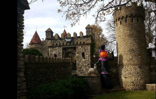 A stone castle with turrets and a decorative inflatable figure in a garden, surrounded by trees and autumn leaves.